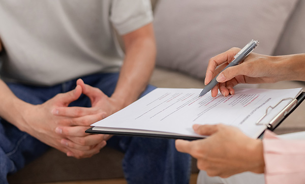 person sitting on a couch with hands clasped while another person writes on a clipboard during a consultation discussing three important topics