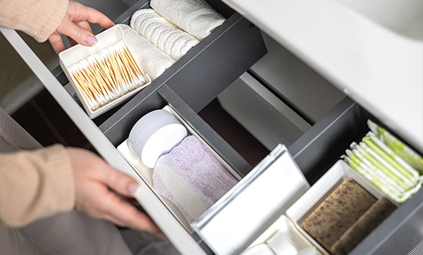 person organizing personal care items in a neatly arranged drawer with various compartments containing cotton pads, sanitary products, and a variety of feminine hygiene essentials for daily use and comfort with eight neatly stored items
