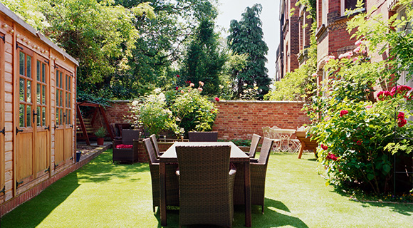 a sunny garden scene featuring a wooden shed vibrant flowers green lawn and outdoor dining set perfect for gatherings