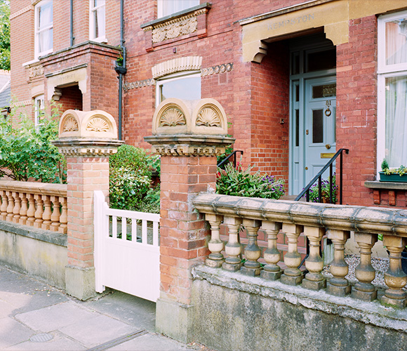 brick house entrance with decorative pillars and a white gate surrounded by greenery featuring two pillars and two gates