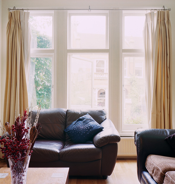 cozy living room with large windows and curtains featuring a leather sofa and decorative pillow highlighting a comfortable atmosphere for relaxation in a stylish home perfect for five people