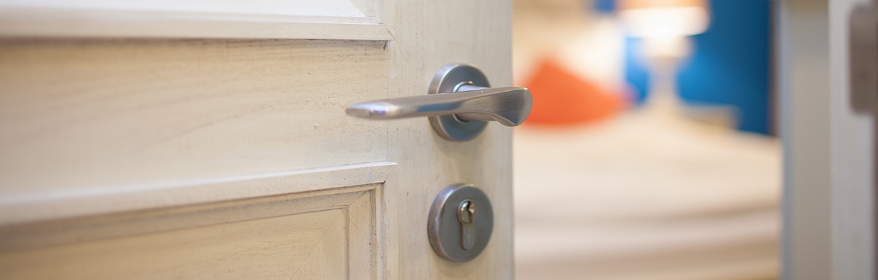 close up of a door handle showing the edge of a room with a blurred background featuring a bed and decorative elements suitable for a cozy space for two guests