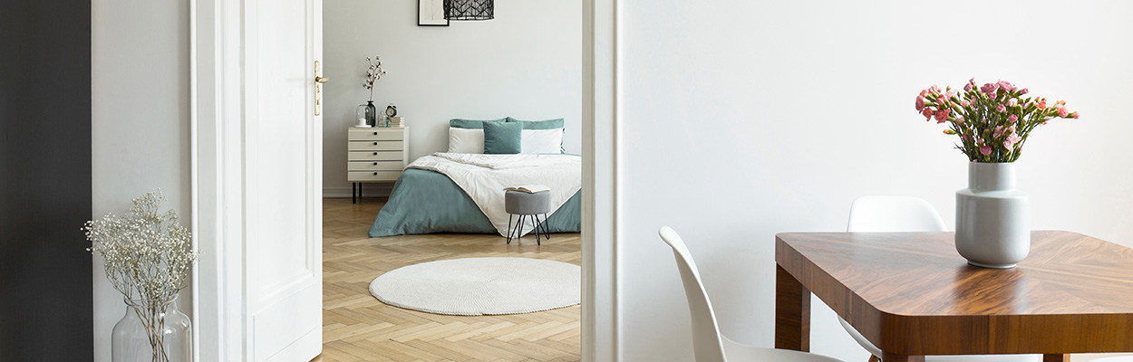 interior view of a modern apartment showing a dining area and a cozy bedroom with turquoise accents and a fresh flower arrangement featuring a round rug and stylish furniture suitable for three spaces