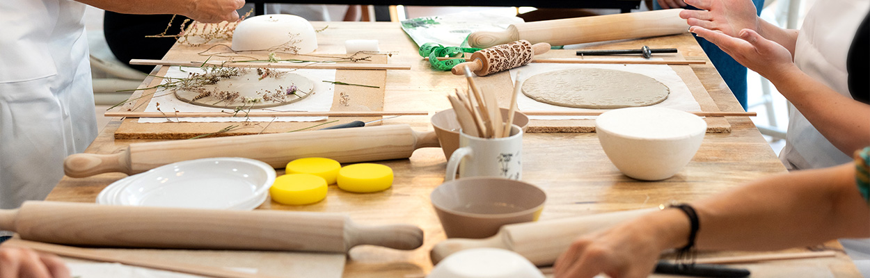 crafting workshop featuring pottery tools and materials with wooden rolling pins and bowls surrounded by participants engaged in creating two unique items