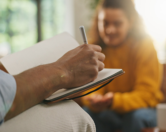 hand writing in notebook with a person sitting nearby in a cozy setting engaging in conversation about two ideas